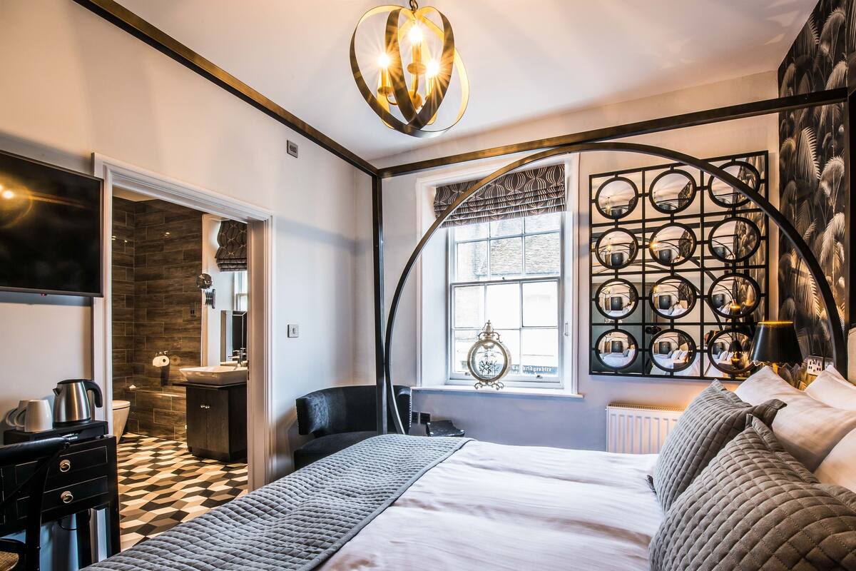 Una habitación de hotel moderna con una cama grande, televisión, baño y una decoración de pared original.
