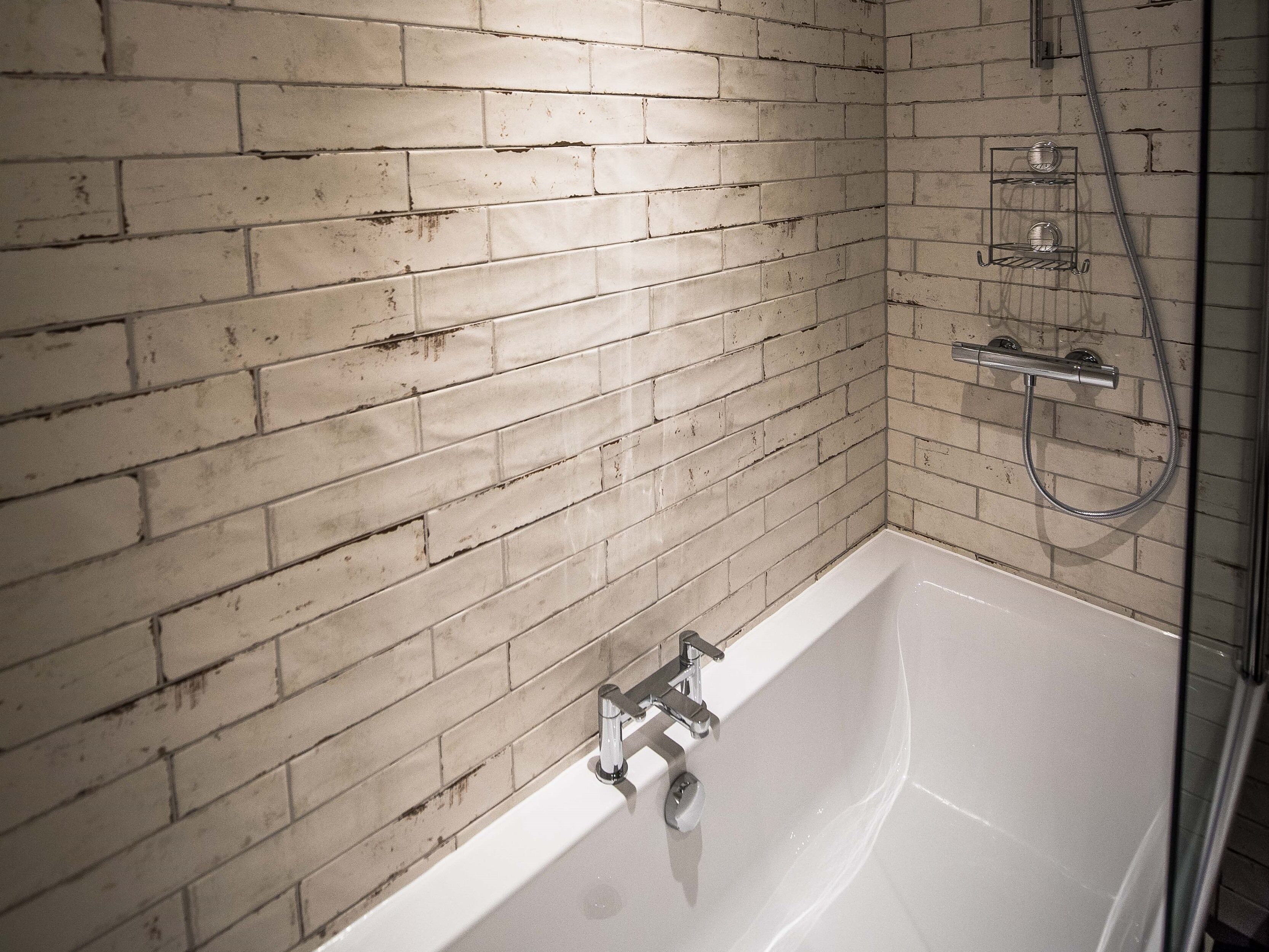 A bathroom with a white bathtub, a shower, and a tiled wall with a brick pattern.