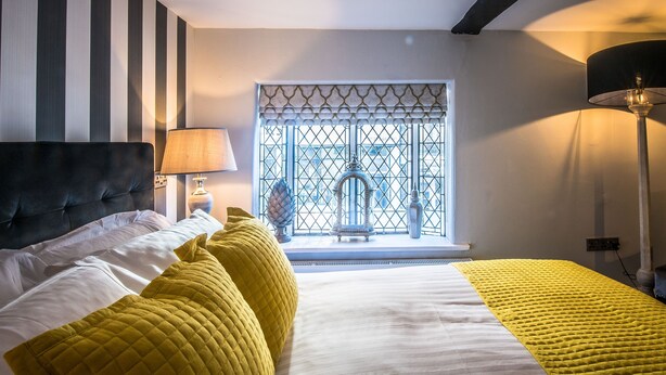 A hotel room with a bed, a lamp, a window with a view, and a decorative item on the windowsill. - The Royal Standard (Ely)