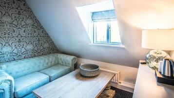 A cozy room with a light blue sofa, a wooden table, a patterned wall, a small window, and a lamp.