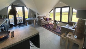 Un loft espacioso con techo alto, zona de comedor, sofá y grandes ventanales con vistas al campo.