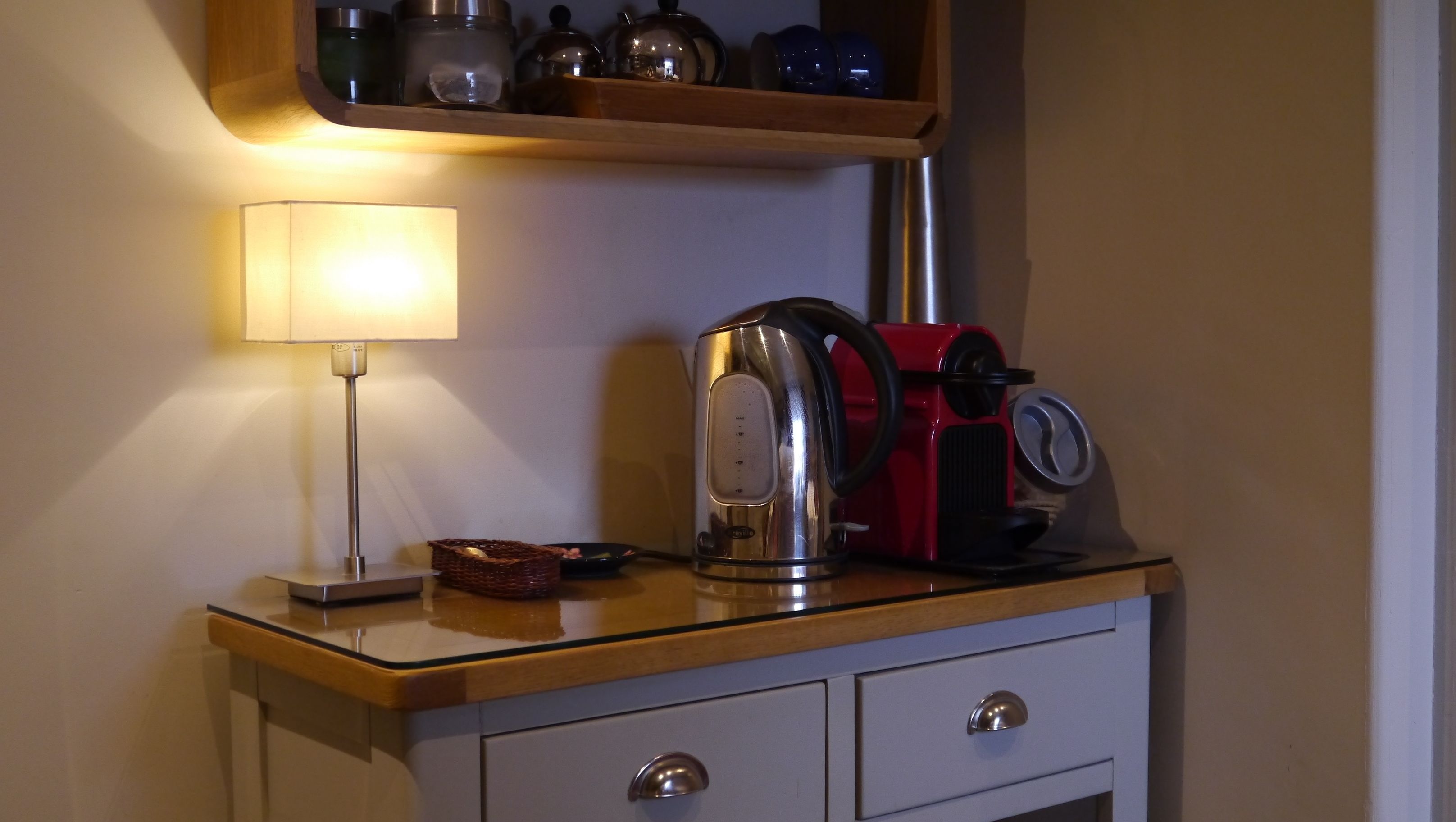 A kitchen counter with a kettle, a red coffee maker, and a lamp.