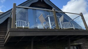 Un edificio de madera con balcón de vidrio, barandillas metálicas y un cielo azul despejado.