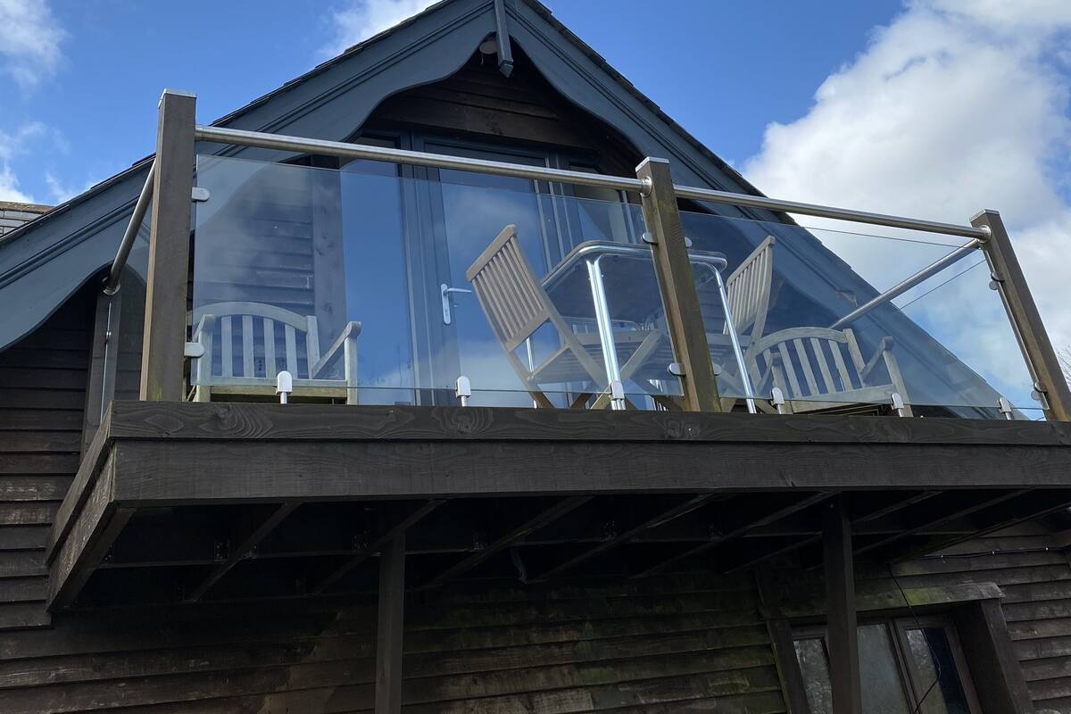 A wooden building with a glass balcony, metal railings, and a clear blue sky.