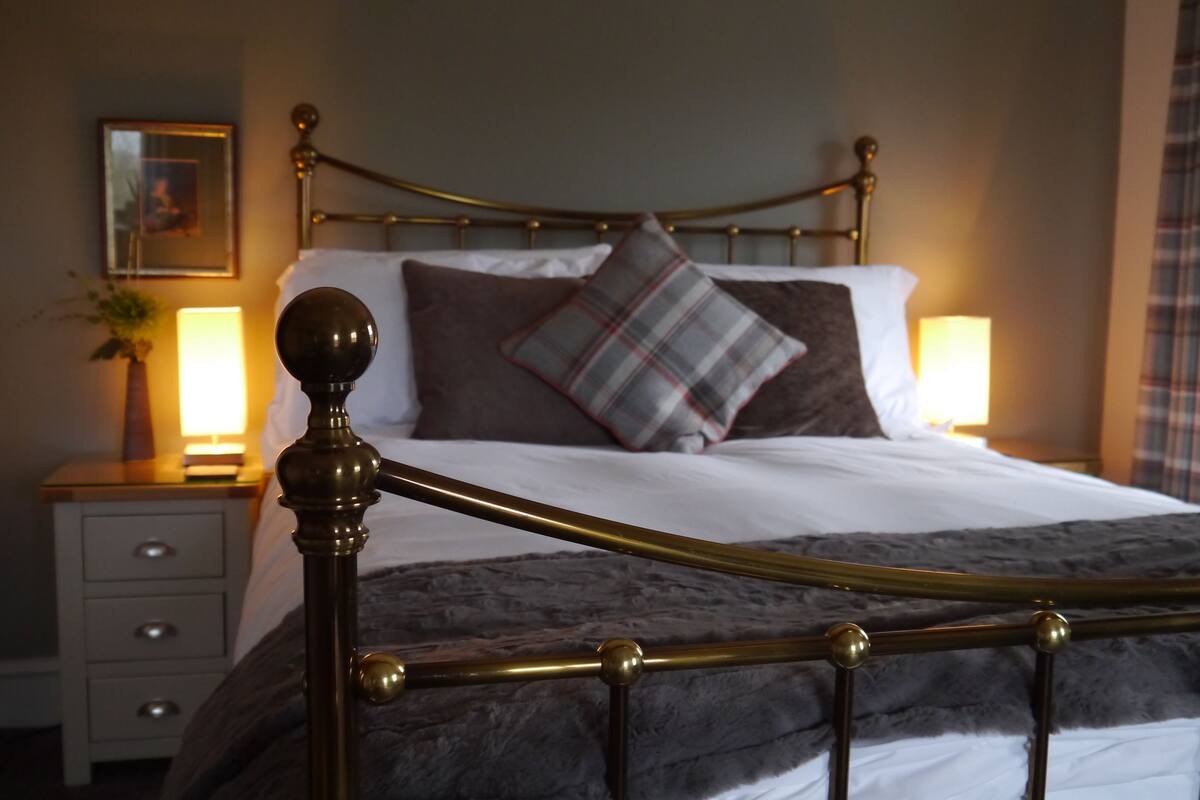 A neatly made bed with a metal headboard, a bedside table with a lamp, and a framed picture on the wall.