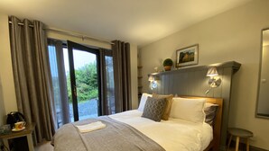 Habitación de hotel con una cama grande, una mesita de noche con lámpara, vistas a zonas verdes y un cuadro en la pared.