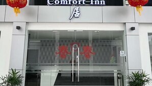 L'ingresso di un hotel con un cartello che riporta “Comfort Inn” e caratteri cinesi sopra. Ci sono due piante in vaso su entrambi i lati dell'ingresso.