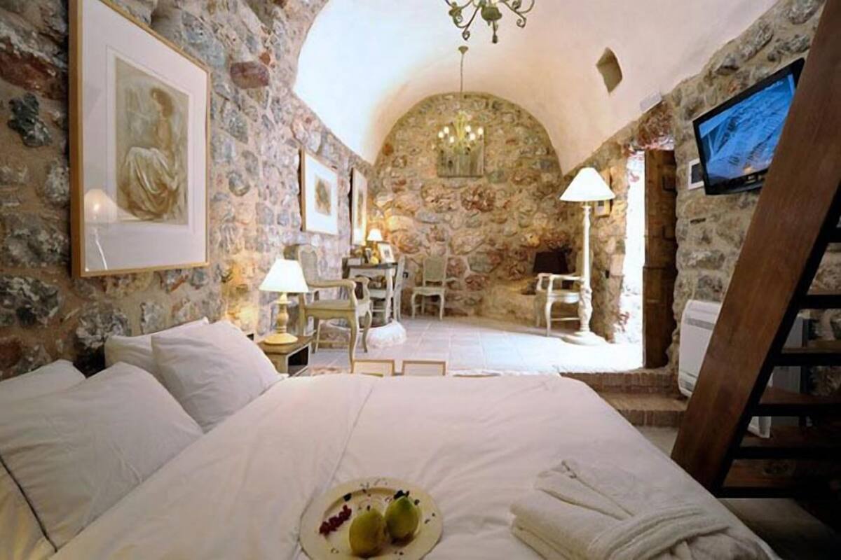 Un dormitorio con paredes de piedra, una cama, un escritorio y un televisor.