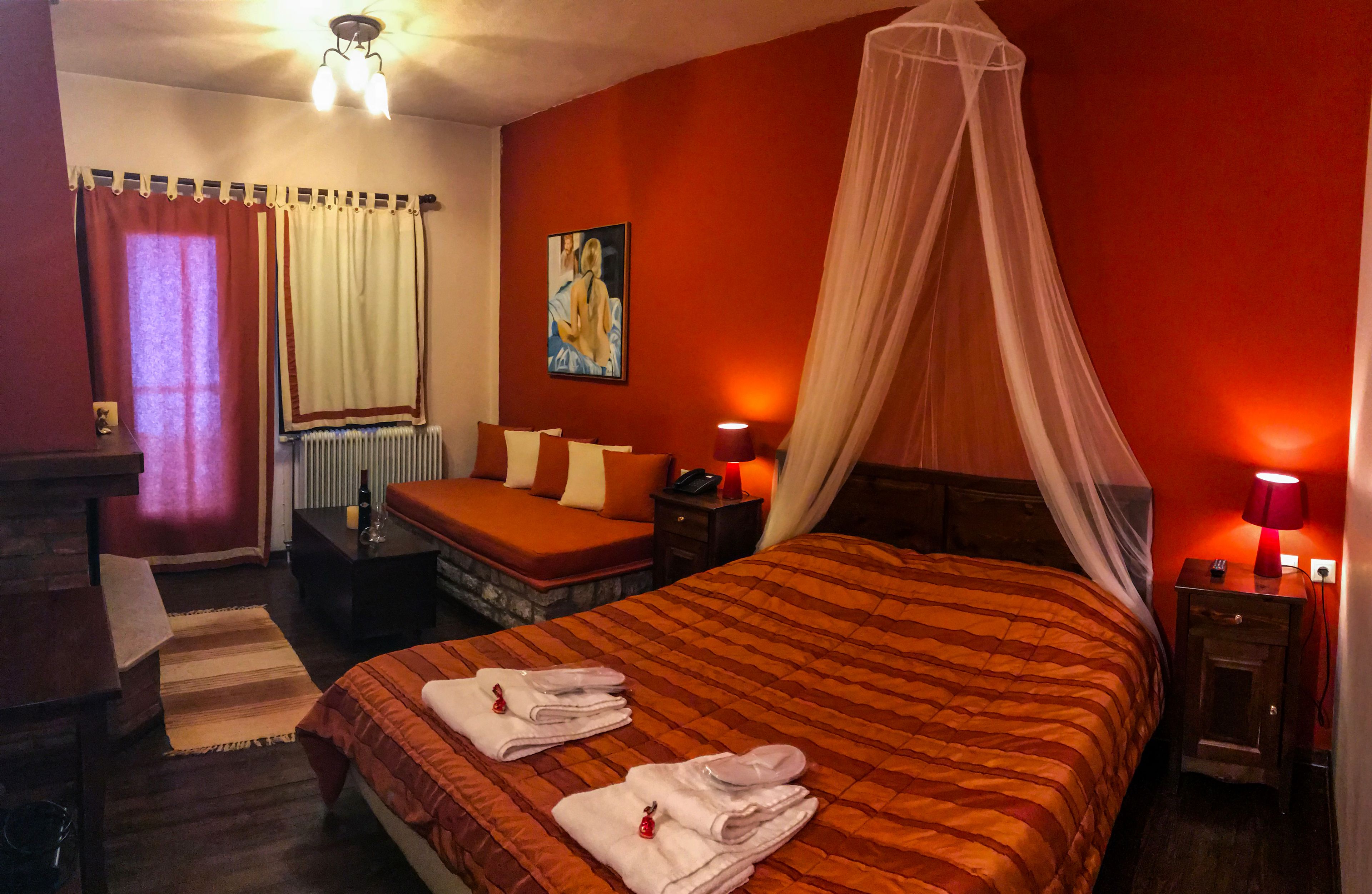 Una habitación de hotel con una cama grande, una mesita de noche con lámpara, una pequeña mesa con una silla, una ventana con cortinas y un cuadro en la pared.