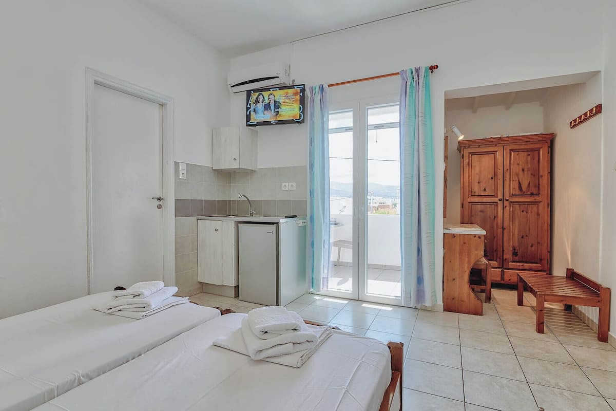 Habitación de hotel con dos camas, kitchenette, armario de madera y balcón con vistas.