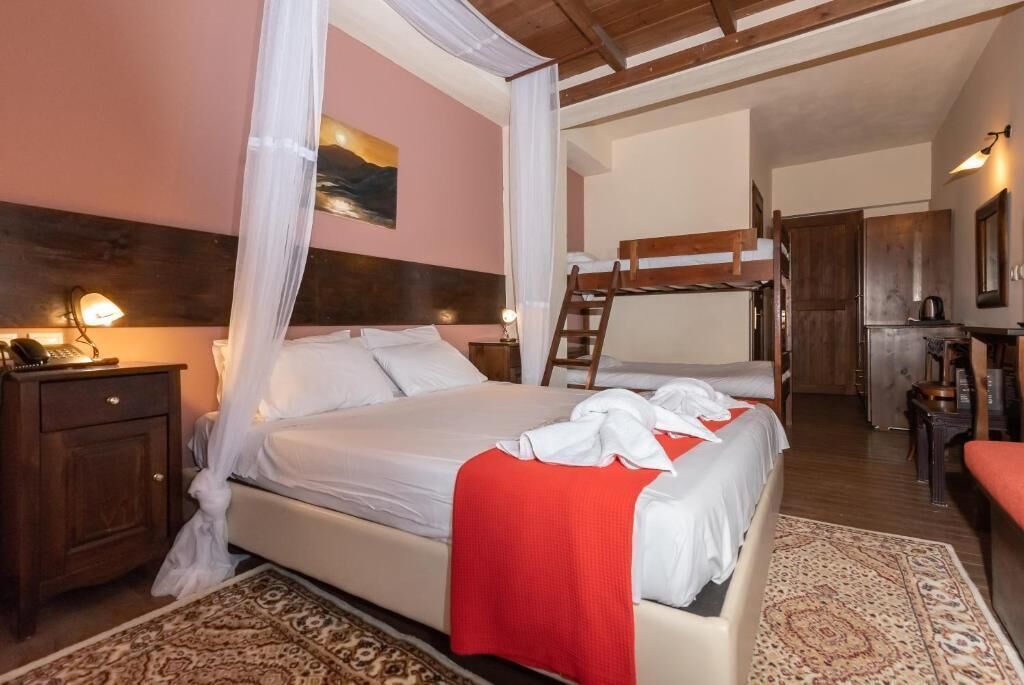 A bedroom with a large bed, a nightstand, a wooden ladder, and a kitchen area visible through an open door.