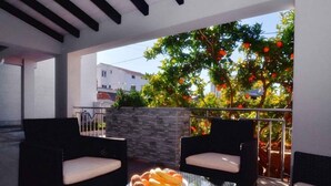 A modern outdoor seating area with two black wicker chairs and a glass table, featuring a bowl of fruit. - Holiday apartment with terrace and air conditioning (Zadar)
