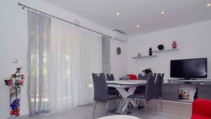 A modern living room with a dining area, a flat-screen TV, and a red sofa. - Holiday apartment with terrace and air conditioning (Zadar)