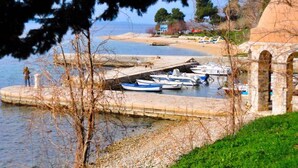 A waterfront area with boats docked at a stone pier, a sandy beach, and a building with arches in the background. - Holiday apartment with terrace and air conditioning (Zadar)