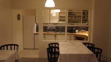 A compact kitchen with a dining area, including a table and chairs, a refrigerator, and a built-in cabinet with dishes.