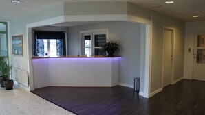 A reception area with a wooden reception desk, a potted plant, and a framed picture on the wall. - Hotell Vindelngallerian (Vindeln)
