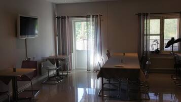 Una habitación amplia con una gran televisión de pantalla plana montada en la pared, una mesa de comedor con sillas, un sofá y una ventana con cortinas.