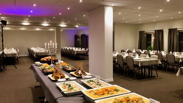 A banquet hall with multiple tables set for dining, featuring various dishes displayed on platters. - Hotell Vindelngallerian (Vindeln)
