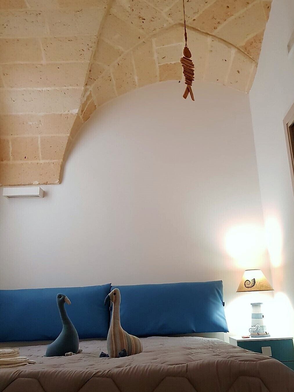 A bedroom with a brick ceiling, a blue headboard, two plush toys on the bed, and a bedside lamp.