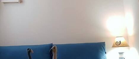 A bedroom with a brick ceiling, a blue headboard, two plush toys on the bed, and a bedside lamp.