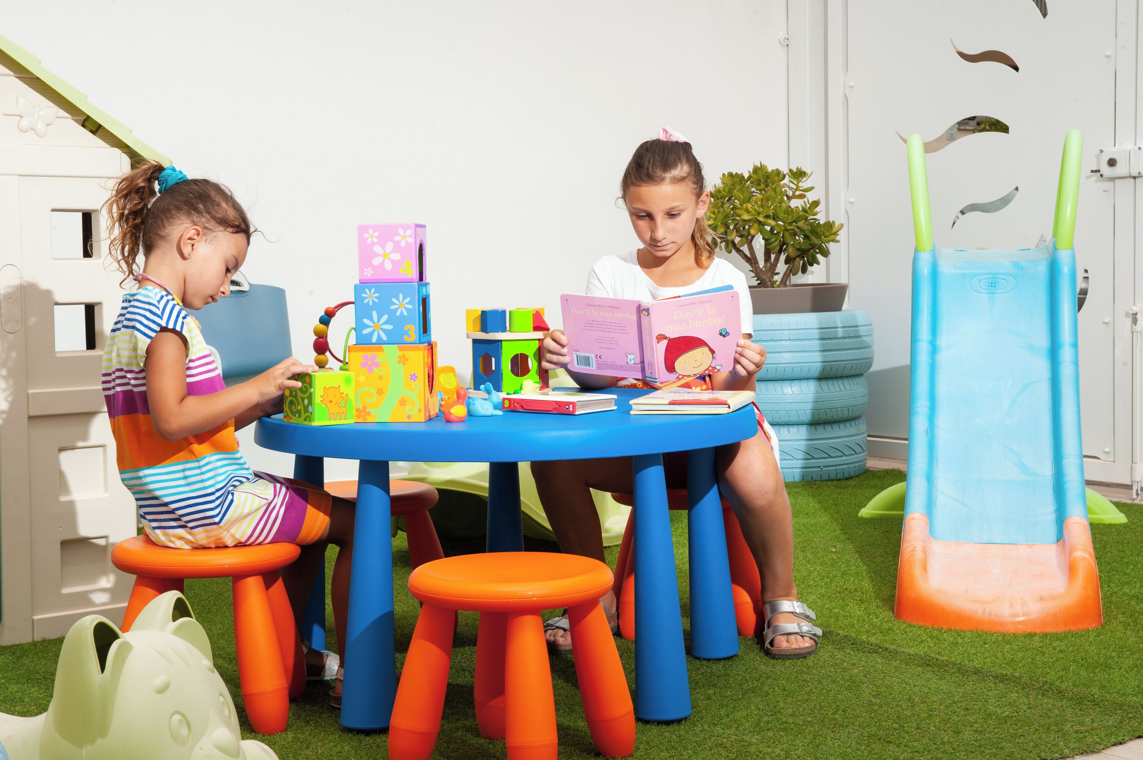 Dos niños sentados en una mesa azul con juguetes y libros de colores.