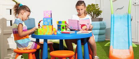 Dos niños sentados en una mesa azul con juguetes y libros de colores.