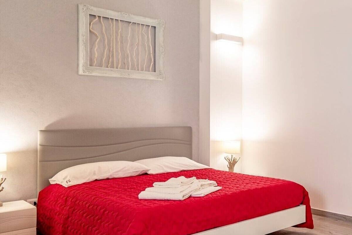 Un dormitorio moderno con un cabecero tapizado en gris, una colcha acolchada roja y dos lámparas de noche.