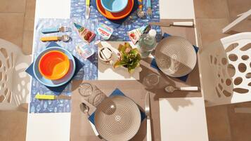 Una mesa de comedor dispuesta con platos, tazones, cubiertos y aderezos.