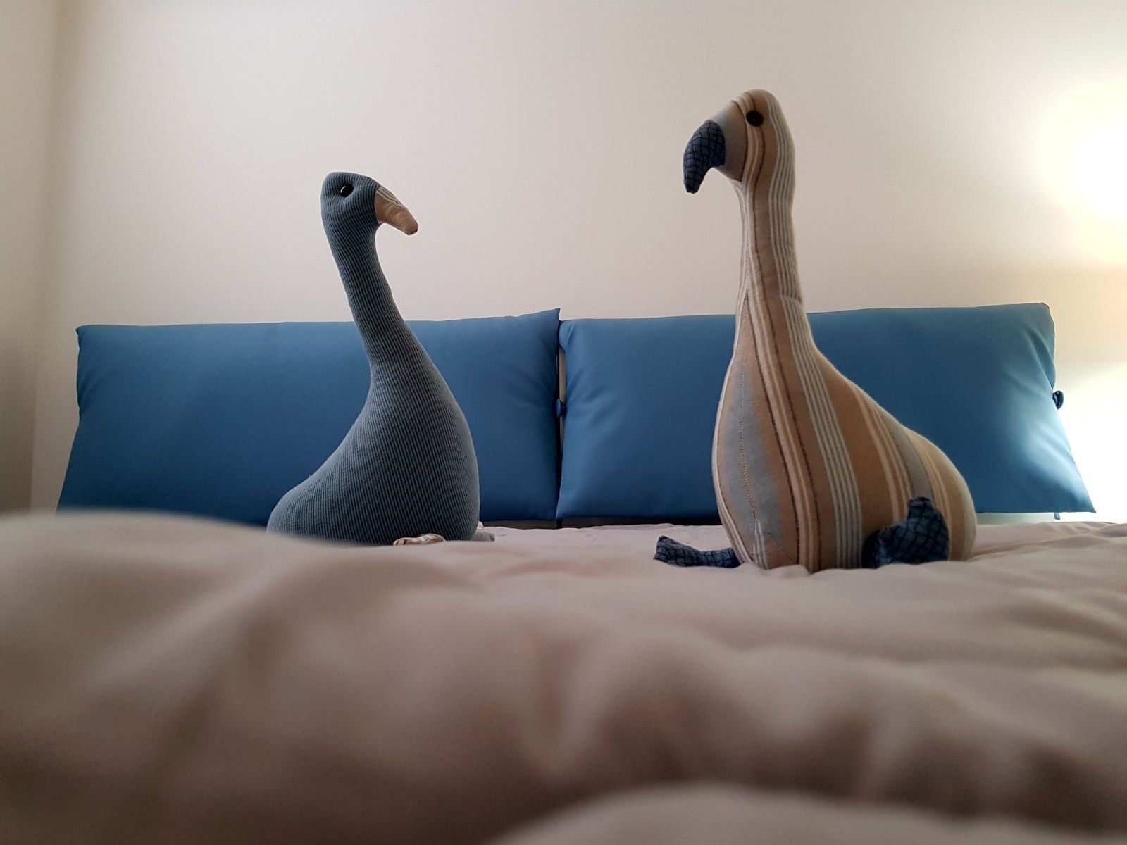 Two decorative bird sculptures on a bed with a blue headboard and pillows.