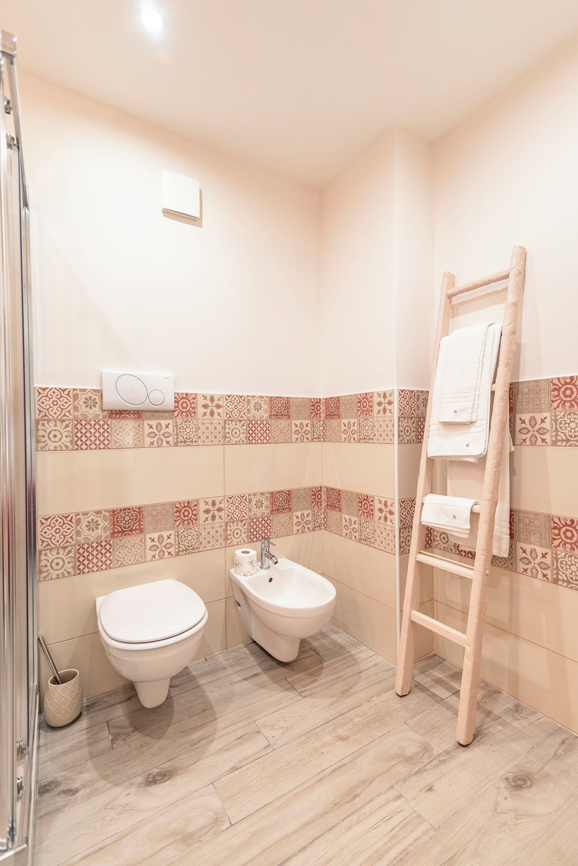 Une salle de bain équipée d’une douche, de toilettes, d’un bidet et d’une échelle en bois sur laquelle sont posées des serviettes.
