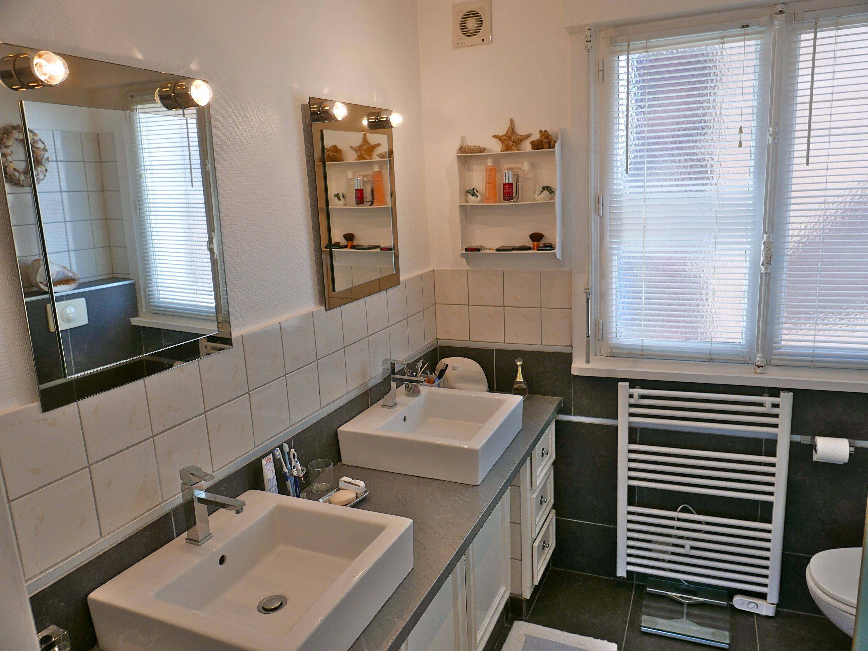 Une salle de bain avec deux lavabos, un miroir et une fenêtre avec des stores.
