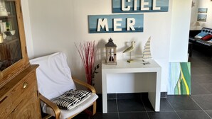 A room with a wooden cabinet, a white chair with a striped cushion, a small table with decorative items, and a wall with the words "CIEL MER" and a painting. - Pleasant house with terrace at 300 m from the sea  (Sangatte)