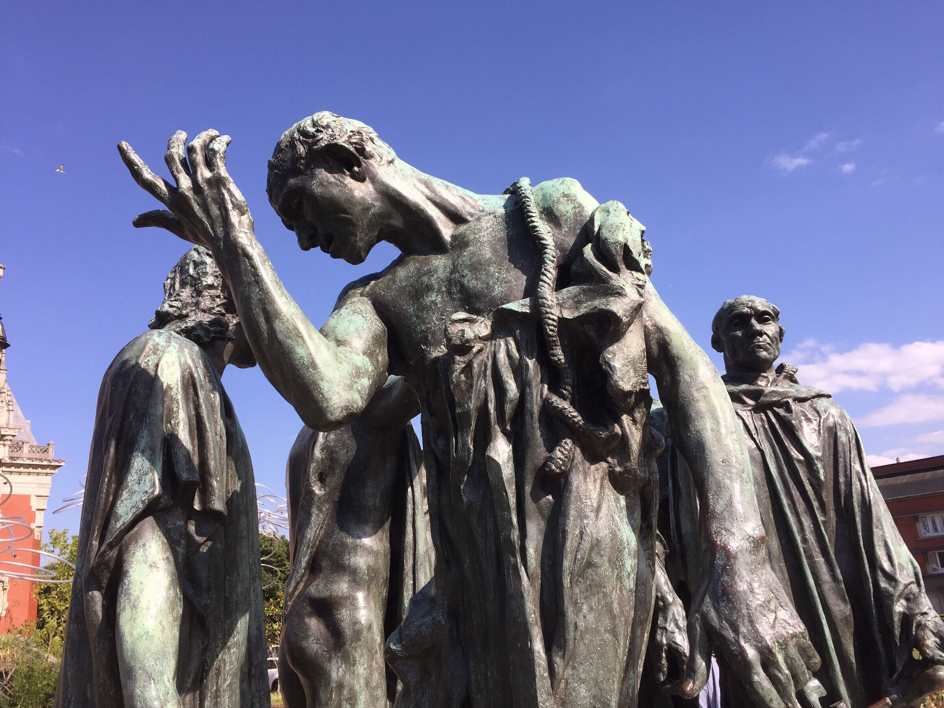 Una estatua de bronce de un hombre en una pose pensativa, con un edificio al fondo.