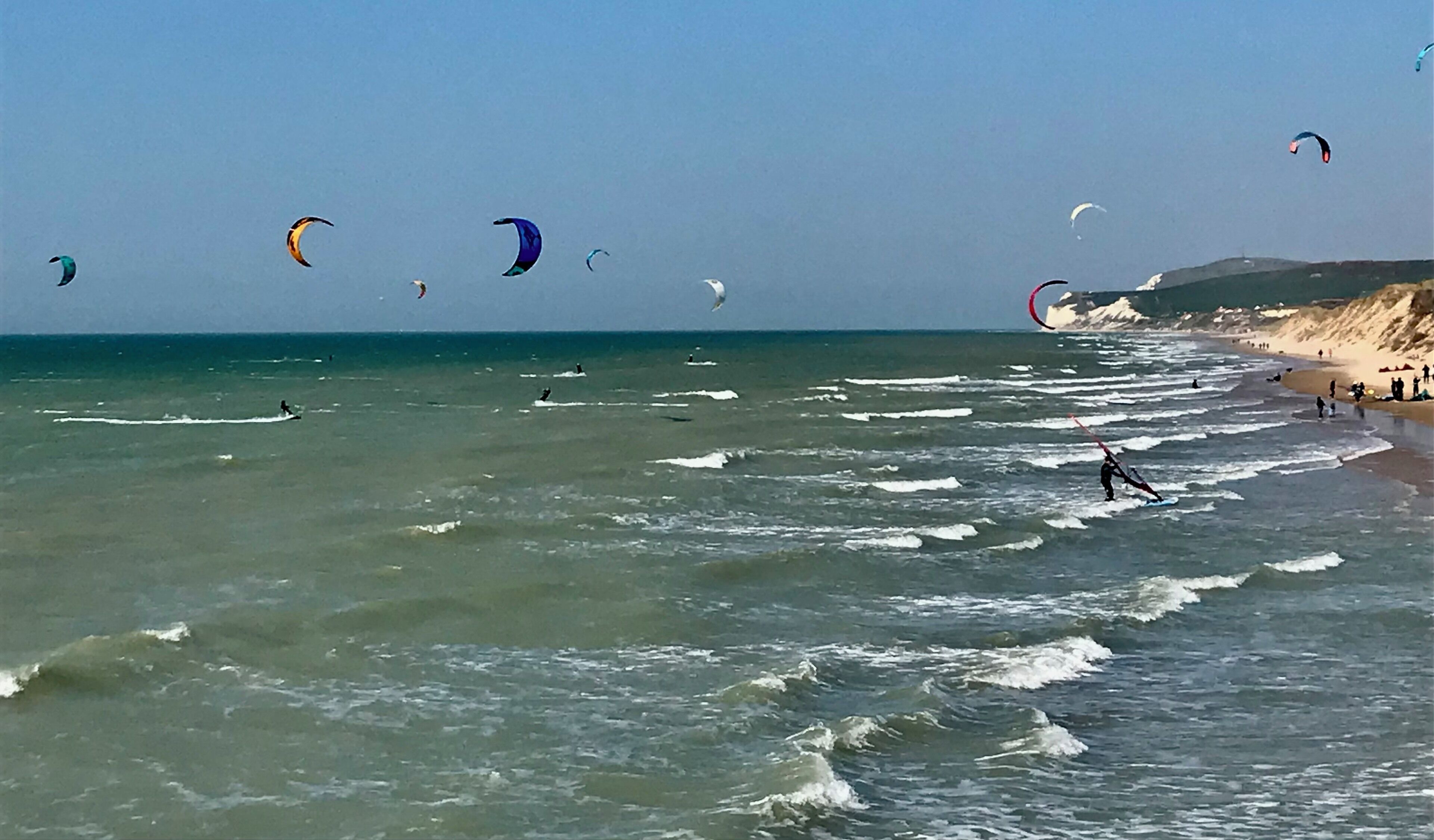 Una playa con varios cometas volando sobre el agua.