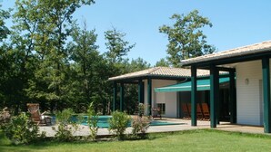 A house with a covered patio, a swimming pool, and a lawn.