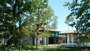 A modern house with a covered patio, a swimming pool, and a well-maintained lawn.