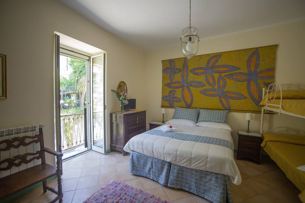 A bedroom with a bed, a bench, a dresser, a painting, and a window.