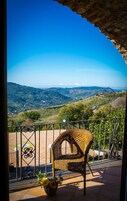 Una silla de mimbre en un balcón con vistas a colinas onduladas y un cielo azul despejado.