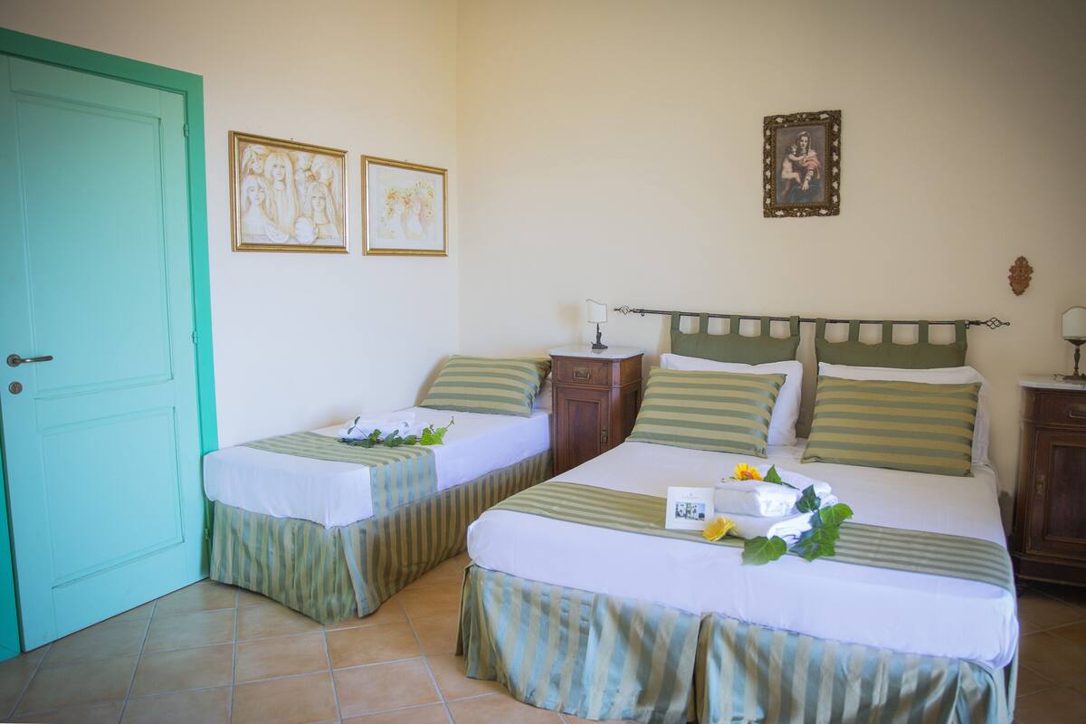 A room with two single beds, a wooden nightstand, a green door, and two framed pictures on the wall.
