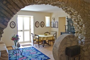 Un comedor con mesa y sillas, un jarrón con flores y un arco de piedra.