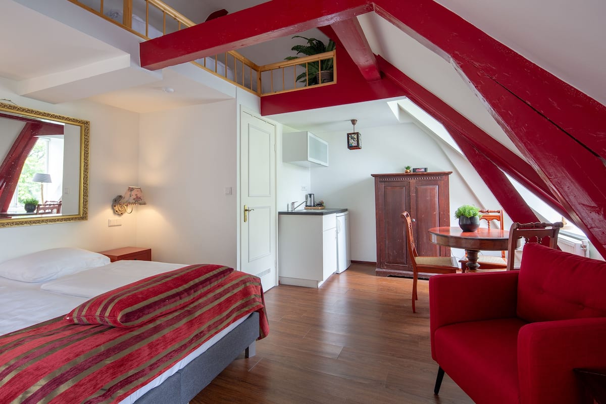 A bedroom with a bed, a red sofa, a dining table, and a kitchen area.