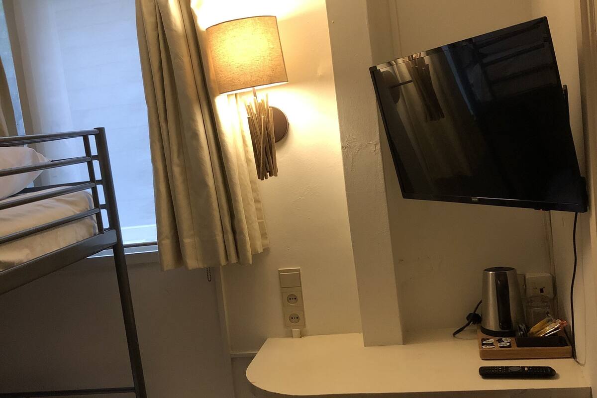 A compact hotel room with a bunk bed, a desk with a flat-screen TV, a lamp, and a coffee maker.