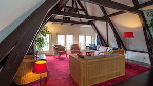A loft-style room with a red carpet, wicker furniture, and a red floor lamp. - Amsterdam House Hotel (Amsterdam)