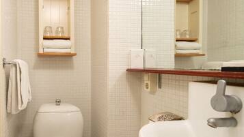 A bathroom with a toilet, sink, and mirror. There are shelves with towels and toiletries.