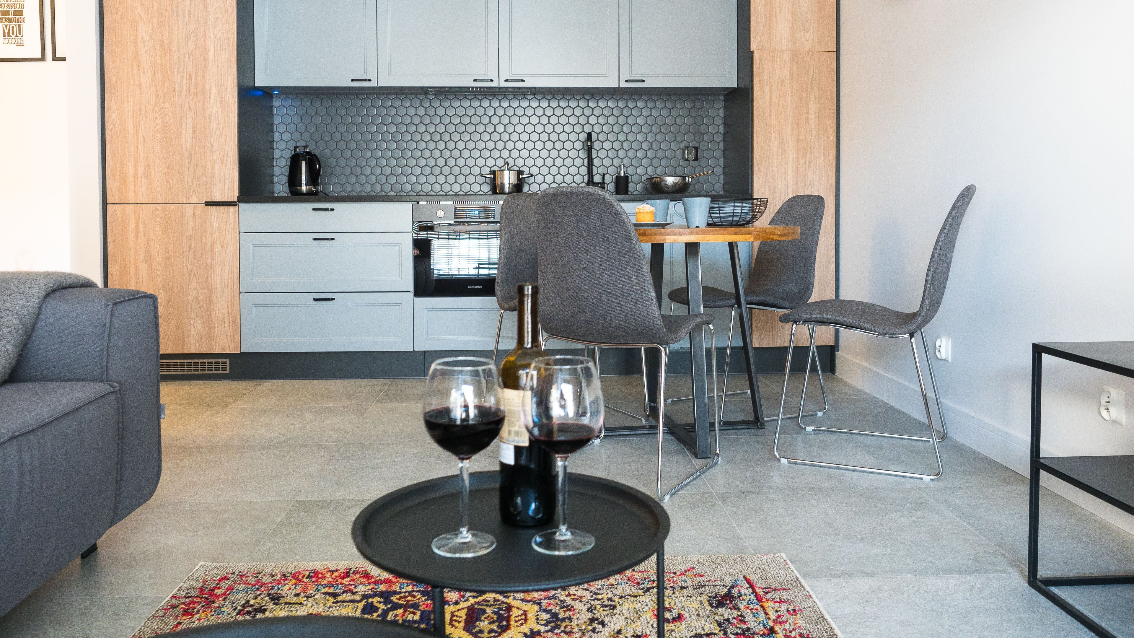 Una cocina moderna con armarios grises, un salpicadero hexagonal y una zona de comedor con una mesa de madera y sillas grises.