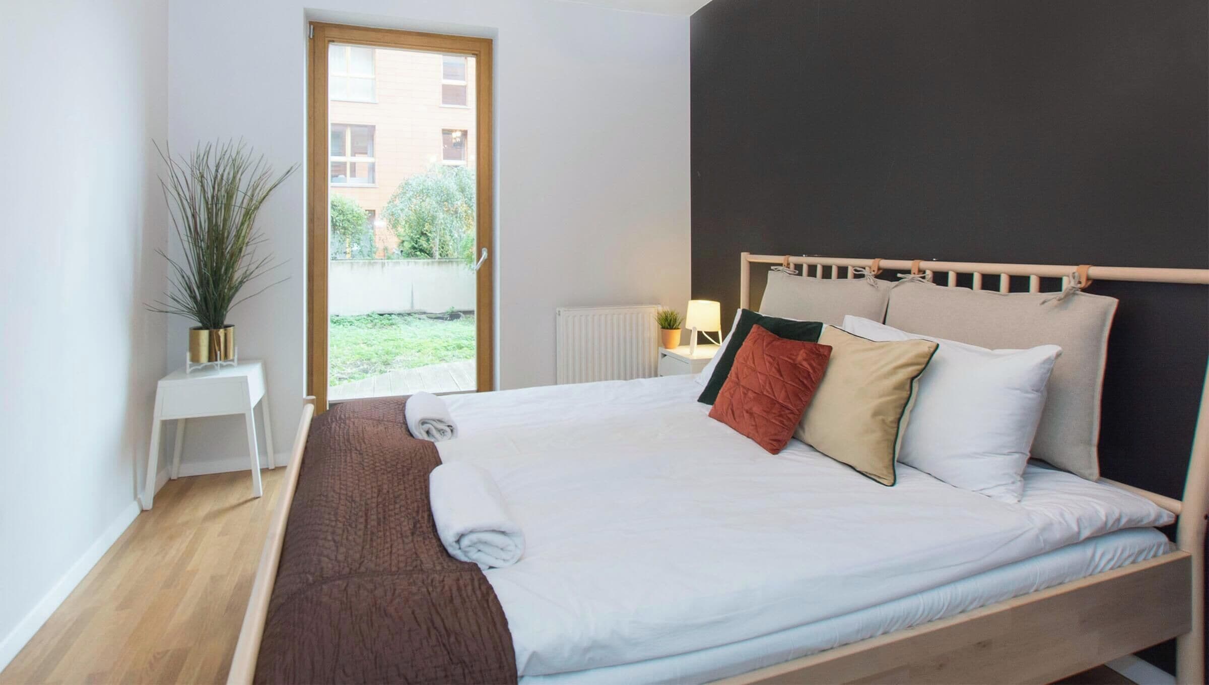 Une chambre à coucher avec un lit, une table de chevet, une lampe, une fenêtre et une vue sur l’extérieur.