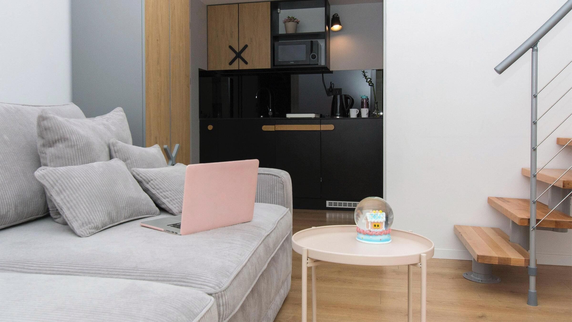 Un salon moderne avec un canapé gris, une petite table ronde agrémentée d’un objet décoratif, et un coin cuisine doté de meubles noirs et d’un four à micro-ondes.