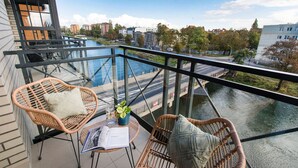 A balcony with wicker chairs, a small table with a book and a glass, overlooking a river and cityscape. - City Center Apartments SPA & Wellness by Apartmore (Gdansk)