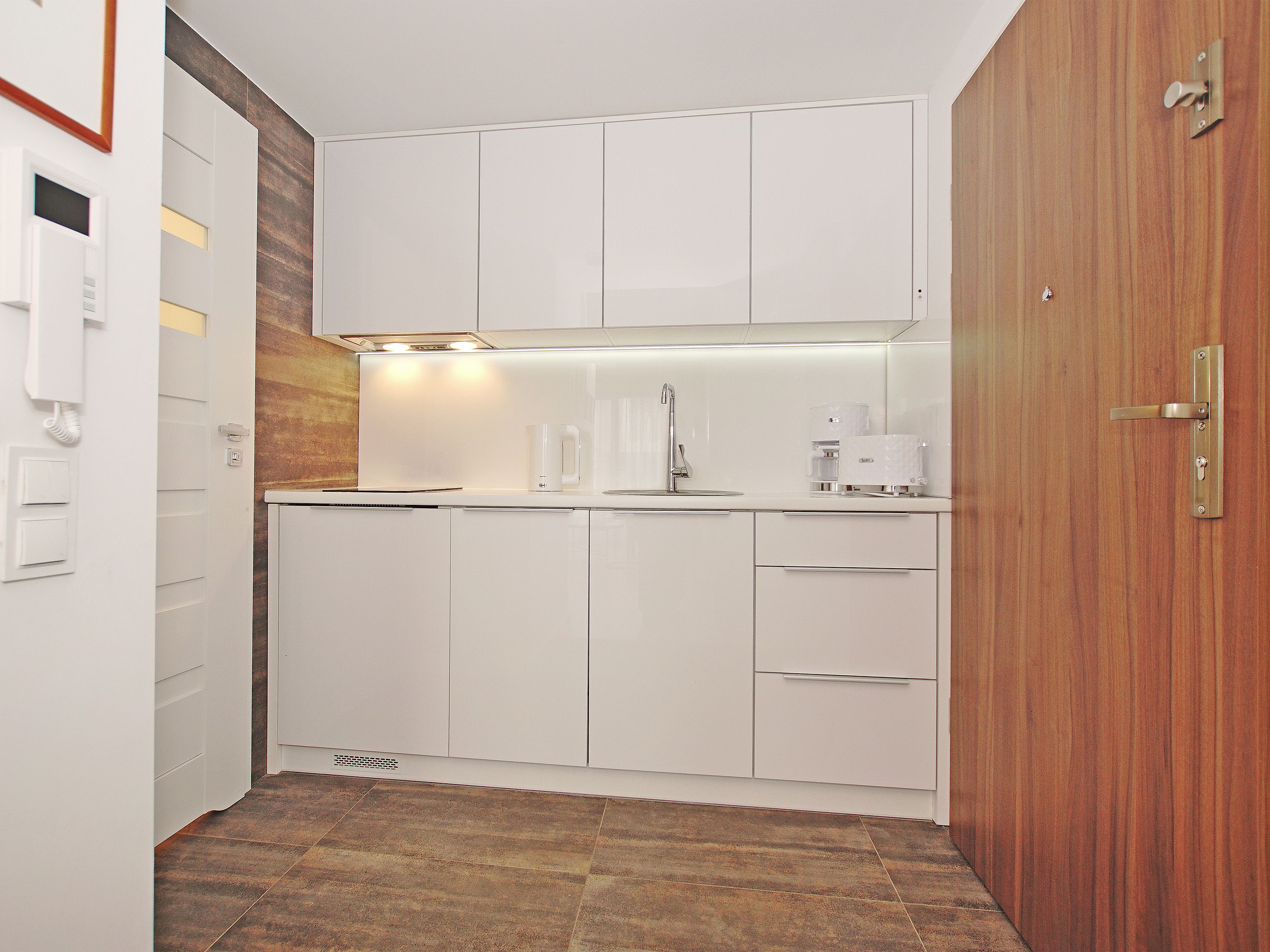 Una cocina compacta con armarios blancos, una puerta de madera y una cafetera.