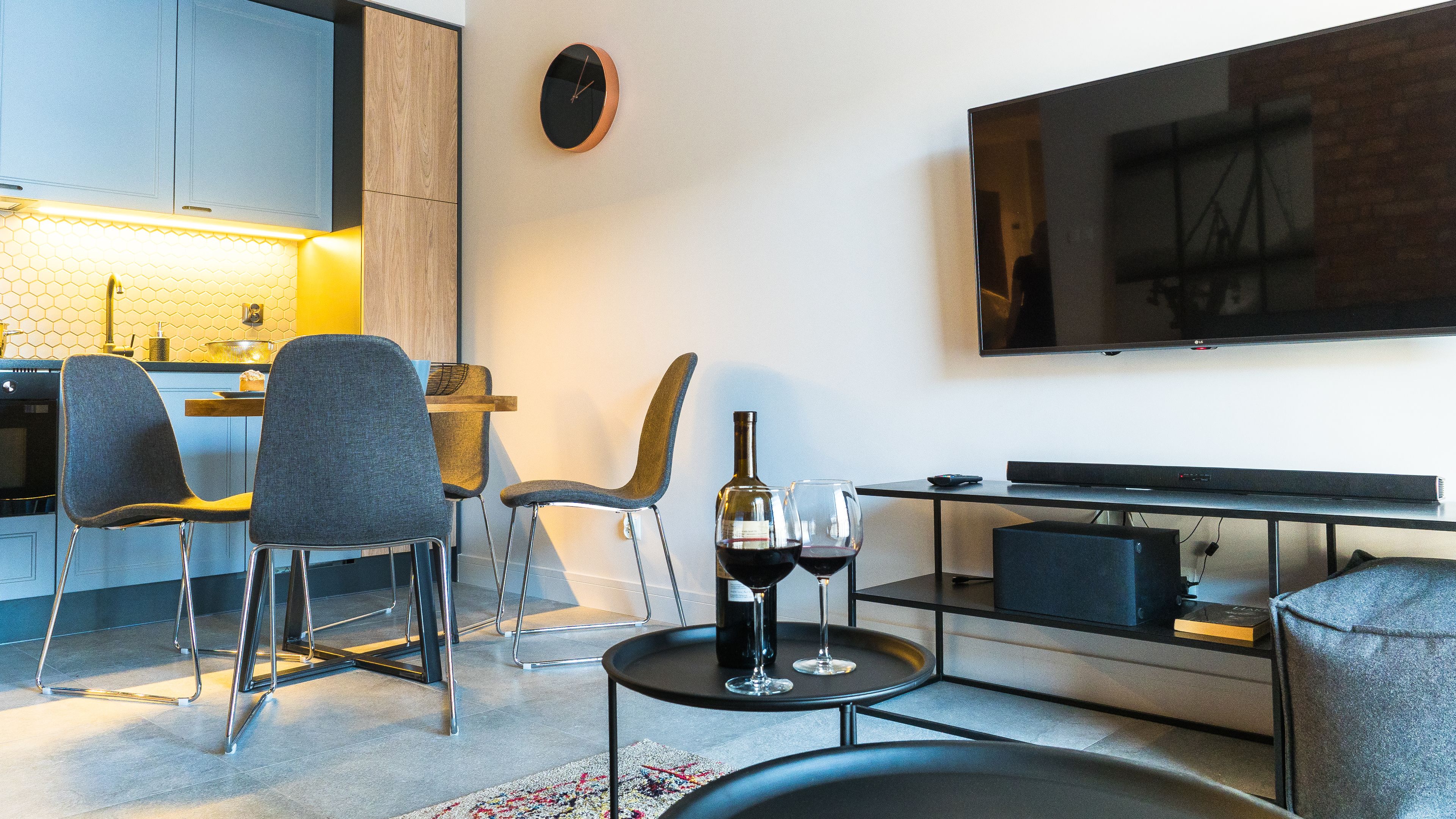 Un salon moderne doté d’un téléviseur à écran plat, d’un coin repas avec une table et des chaises en bois, et d’une cuisine équipée de placards et d’un plan de travail.